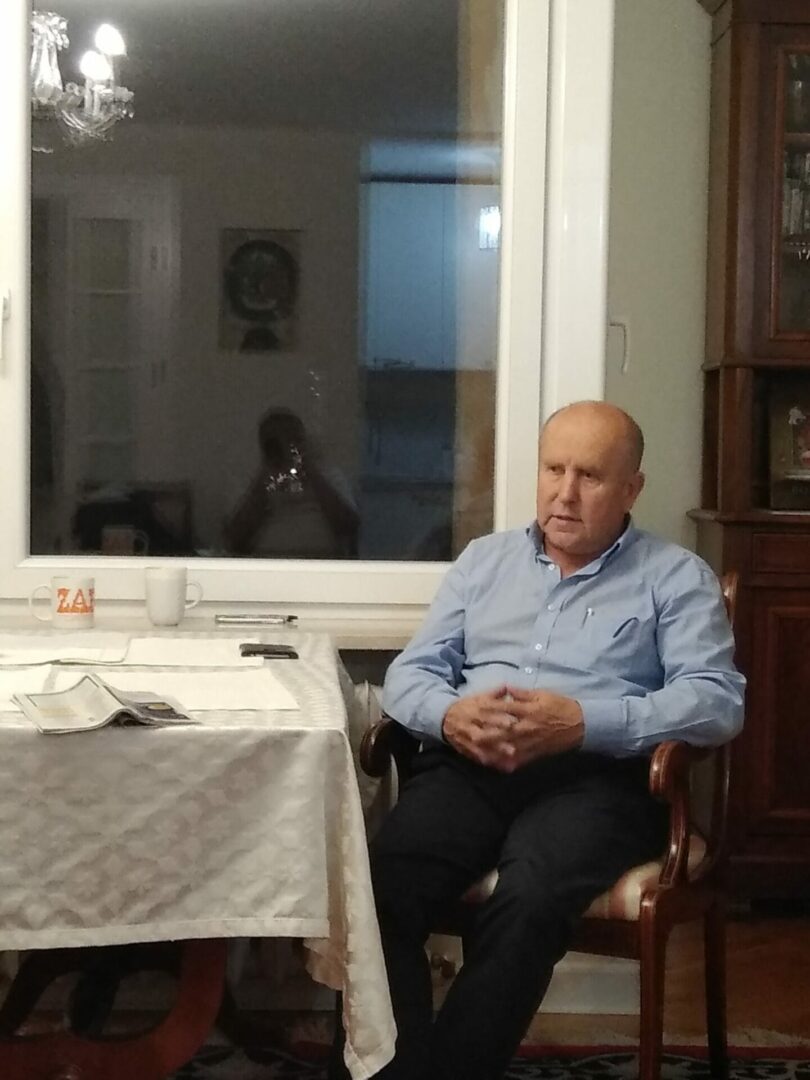 Starszy mężczyzna siedzi na krześle i zamyślony patrzy w kamerę.