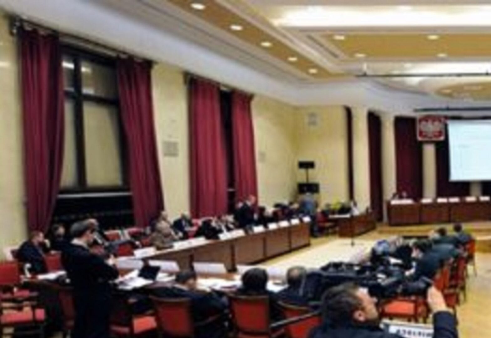 Duża sala konferencyjna, w której uczestnicy siedzą przy długich stołach, dyskutując i współpracując.