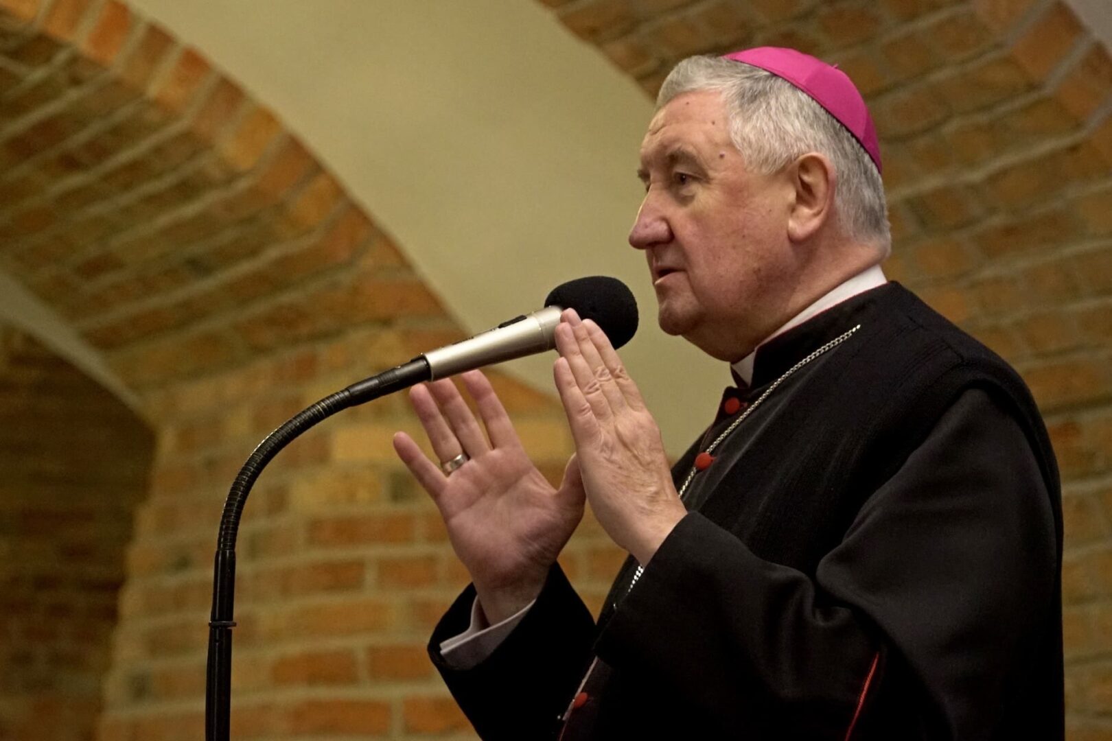 Biskup przemawia do mikrofonu, gestykulując