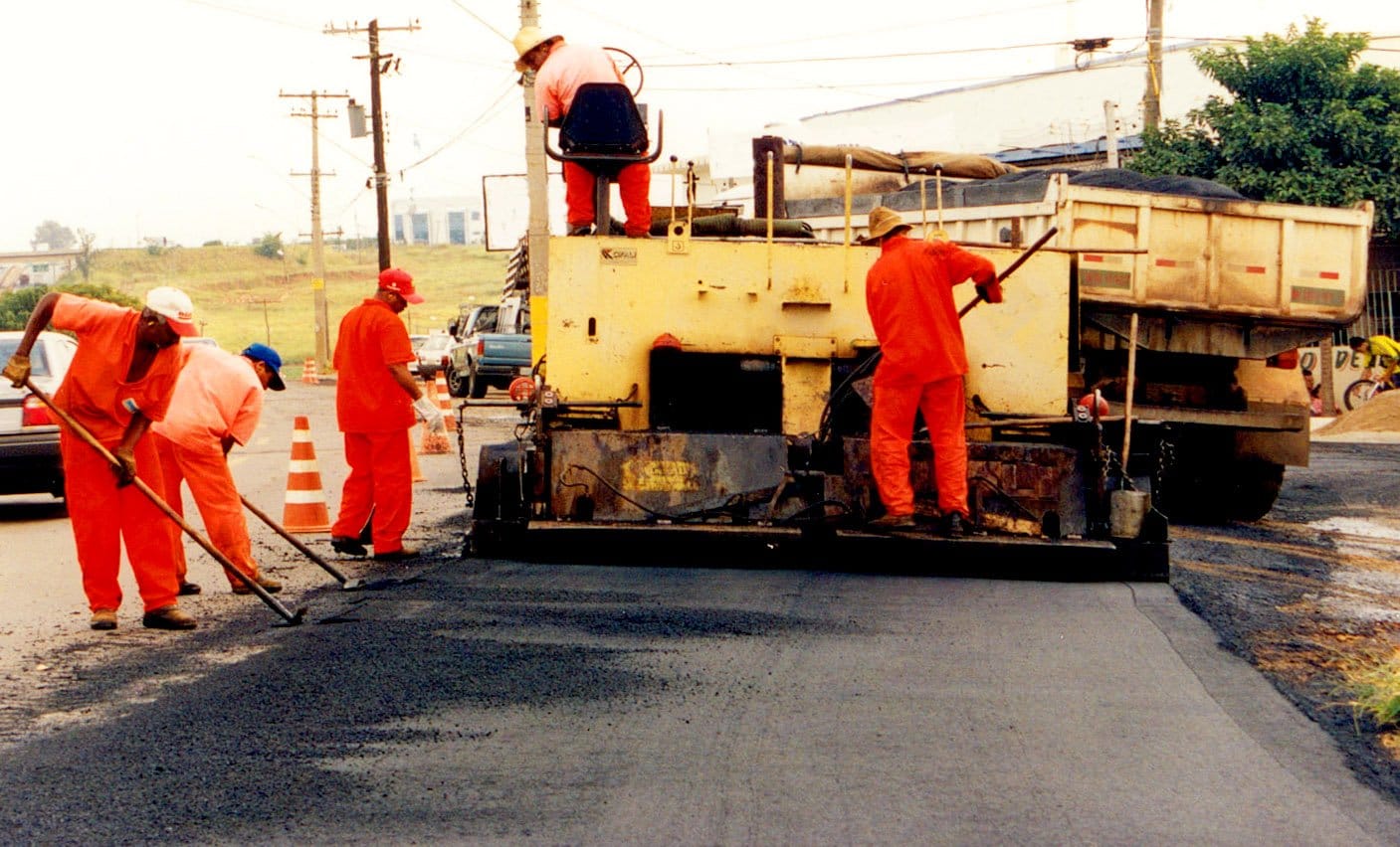 Robotnicy drogowi układają asfalt przy użyciu maszyny do układania asfaltu i narzędzi ręcznych.