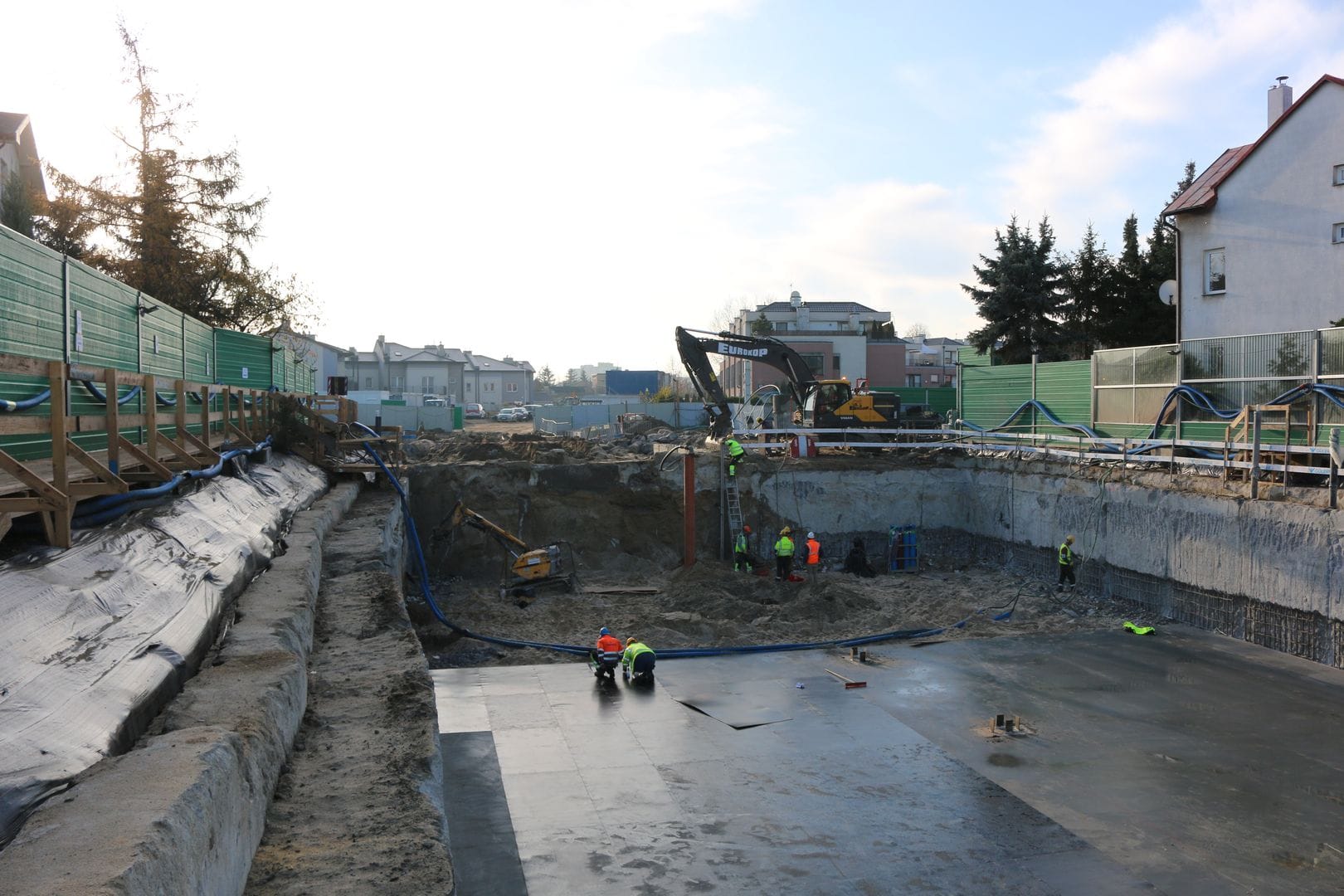 Pracownicy budowlani budujący fundamenty. Koparka i inny ciężki sprzęt na miejscu.