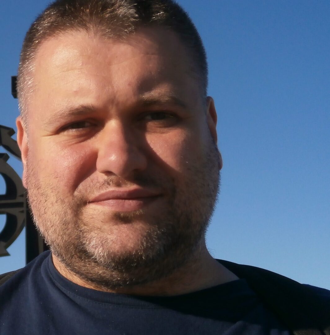 Zdjęcie mężczyzny z krótkimi brązowymi włosami i brodą.