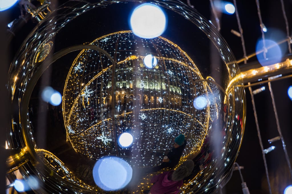 Odblaskowa ozdoba świąteczna przedstawiająca oświetlony budynek i świąteczne światła w nocy.