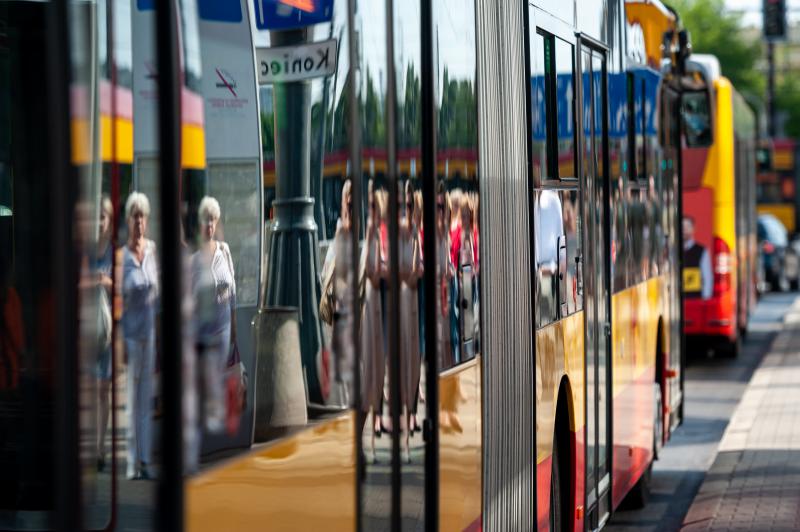 Odbicie ludzi czekających na przystanku autobusowym w mieście, widziane przez okno autobusu komunikacji miejskiej.