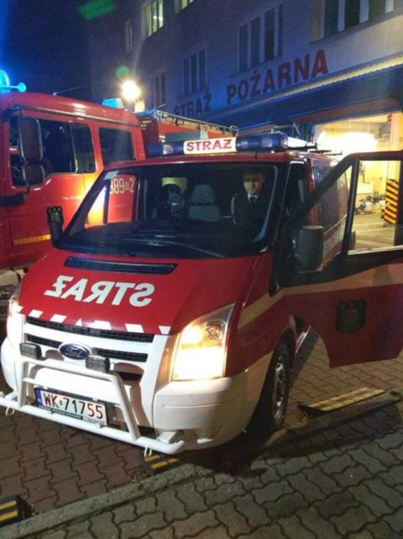 Samochód strażacki Ford Transit zaparkowany nocą przed remizą strażacką. Widoczna „Straż Pożarna”.