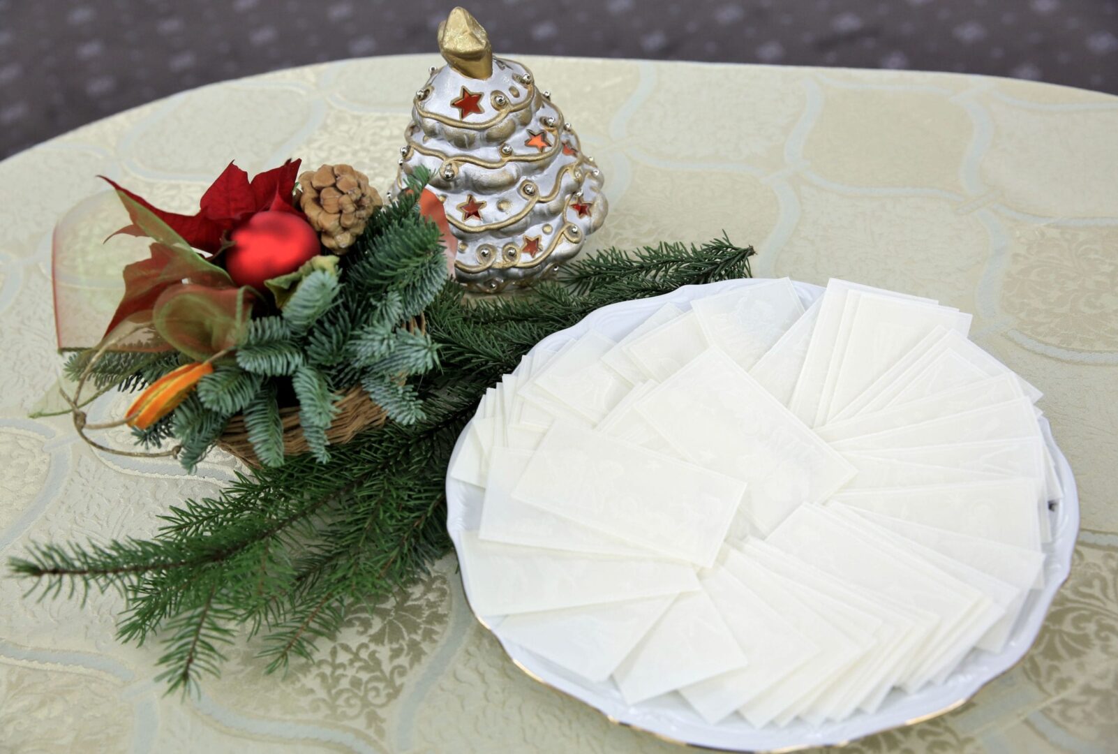 Białe opłatki ułożone na talerzu, obok świątecznej ozdoby.