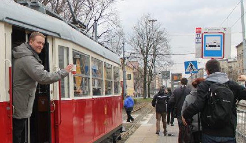 Mężczyzna wsiada do zabytkowego czerwonego tramwaju, tło ulicy miasta