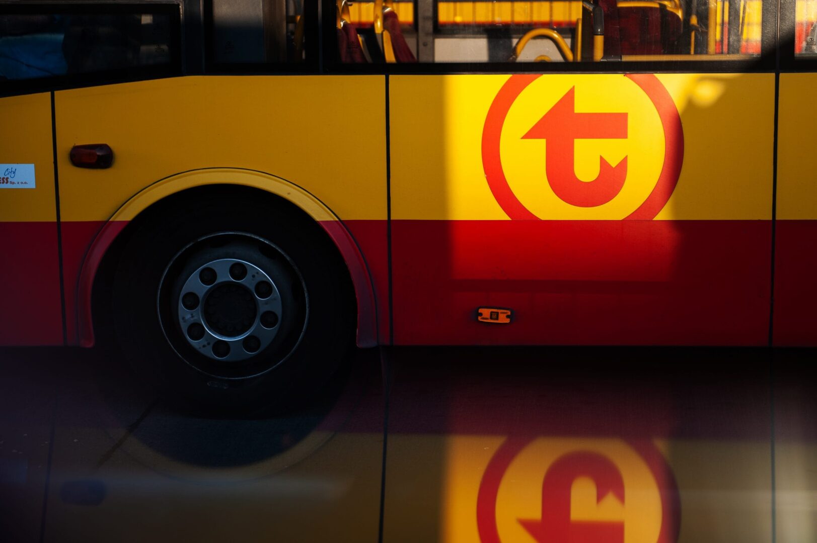 Zbliżenie na żółto-czerwony autobus miejski z widocznym logo w kształcie litery „T”.