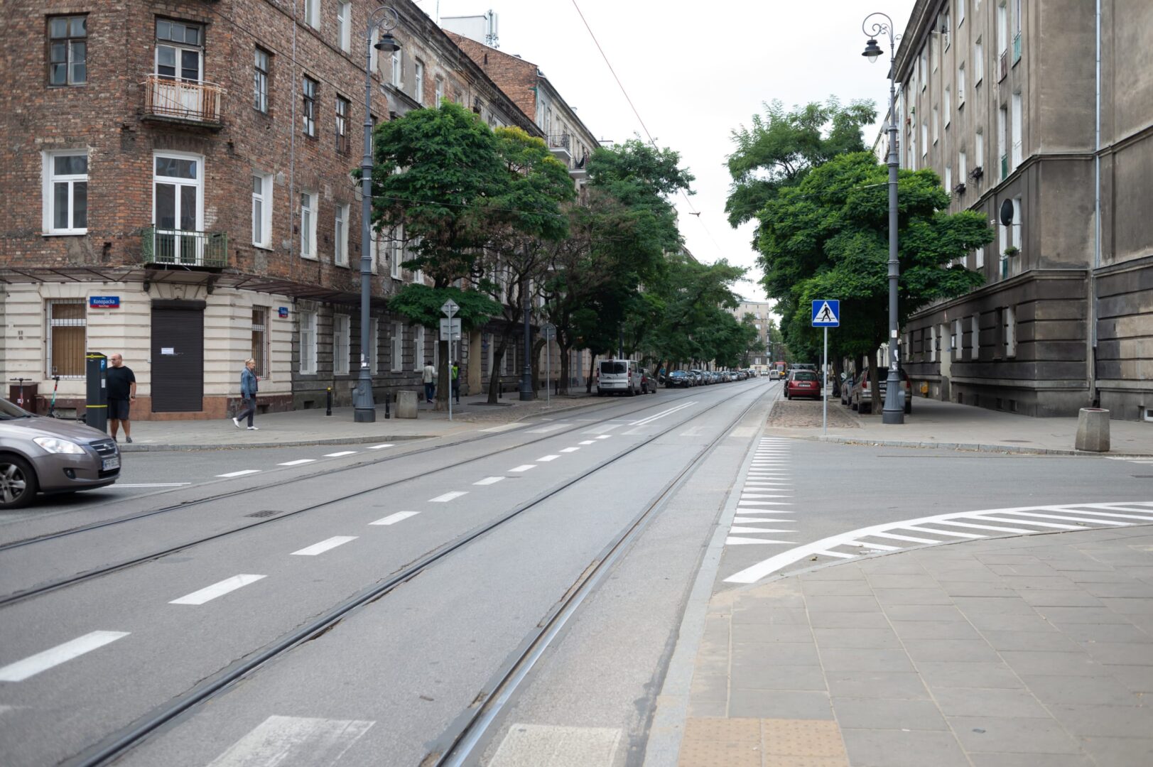 Tory tramwajowe na ulicy obsadzonej drzewami w Łodzi, Polska. Ulicę zdobią ceglane budynki.