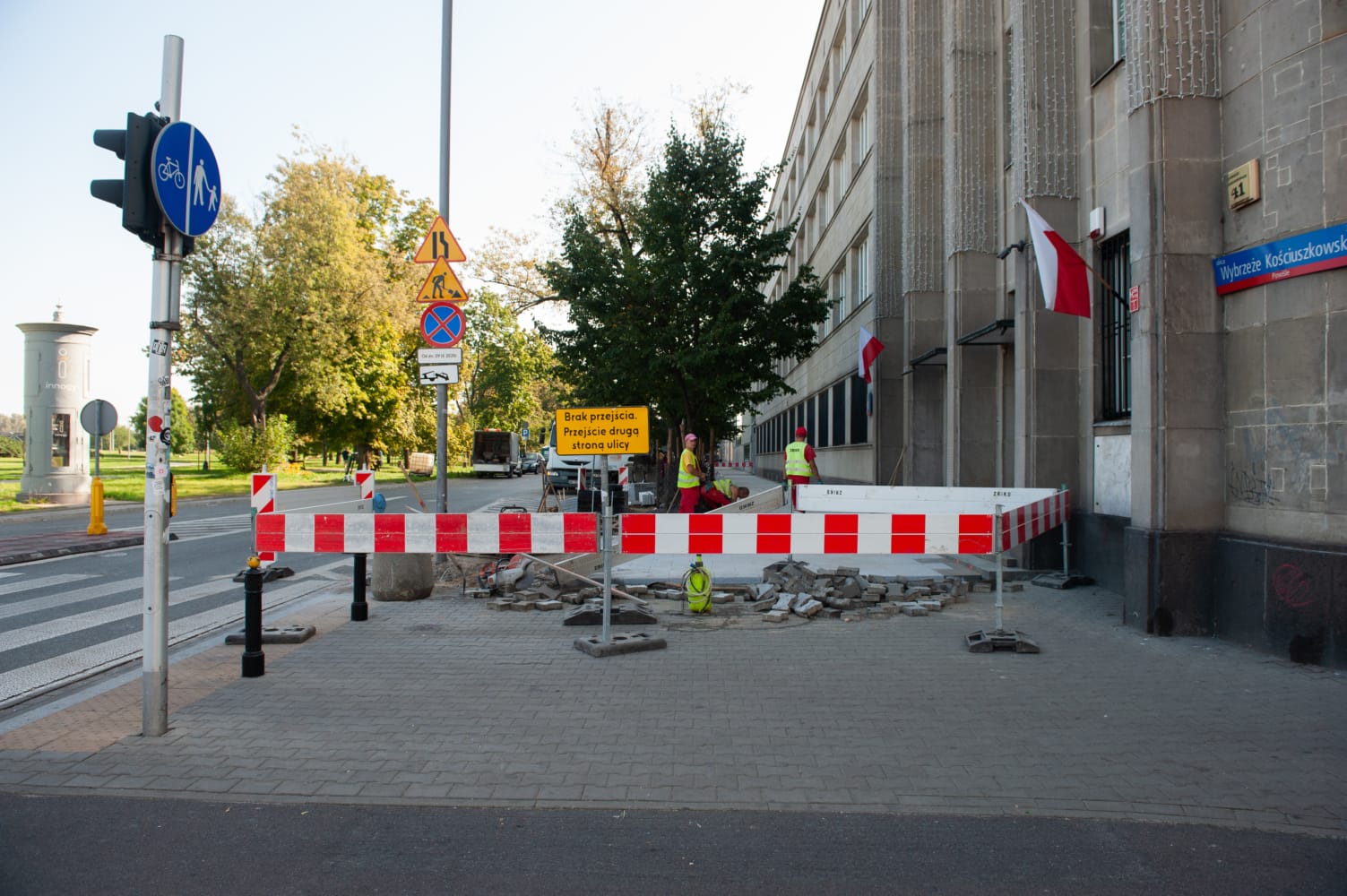 Robotnicy drogowi naprawiający chodnik miejski. Widoczny znak „Brak przejścia”.