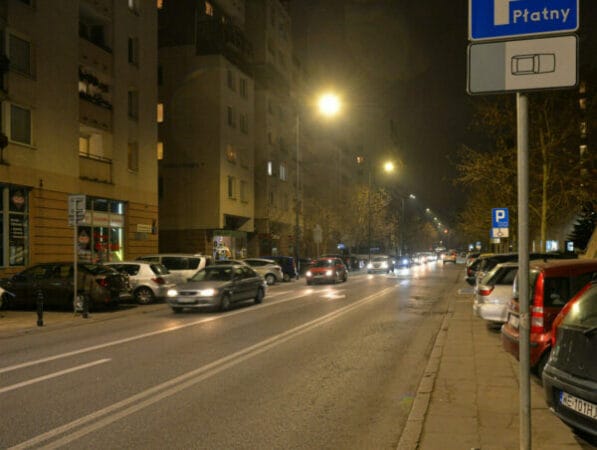 Nocny widok ulicy w mieście, zaparkowane samochody i budynki mieszkalne.