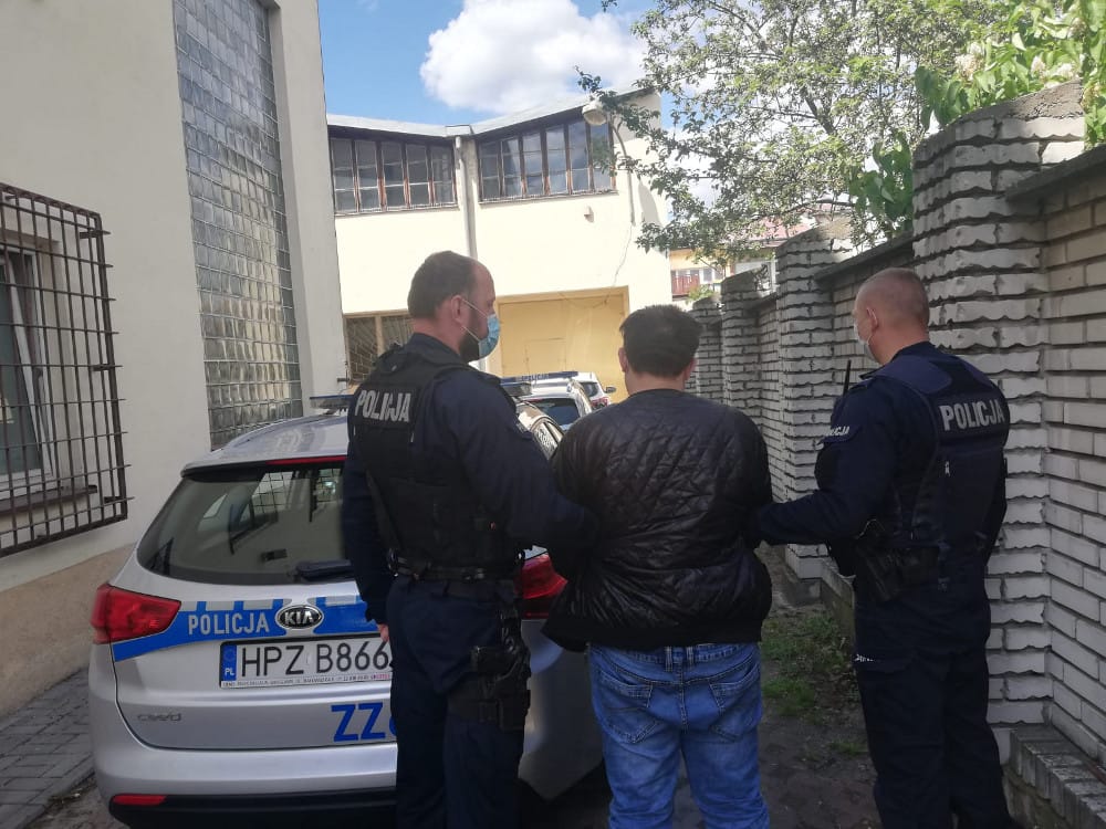 Dwóch polskich policjantów aresztuje podejrzanego w pobliżu radiowozu. Na tablicy rejestracyjnej samochodu widnieje napis „HPZ B866”.