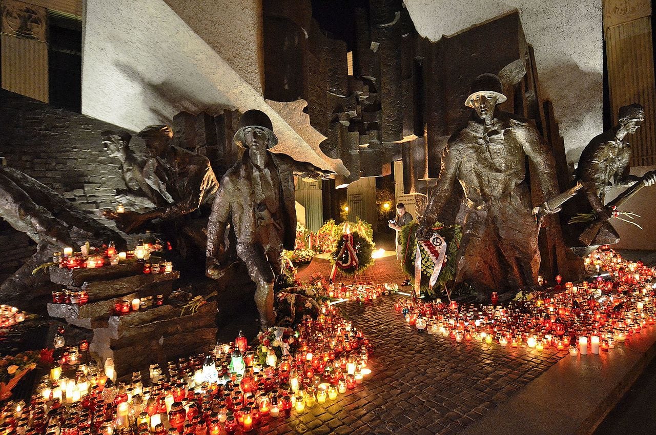 Pomnik Powstania Warszawskiego nocą, oświetlony setkami świec. Rzeźby z brązu przedstawiają żołnierzy.