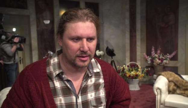 Actor in a red cardigan during a theatrical interview for "Klasyczna farsa w Teatrze Kwadrat".