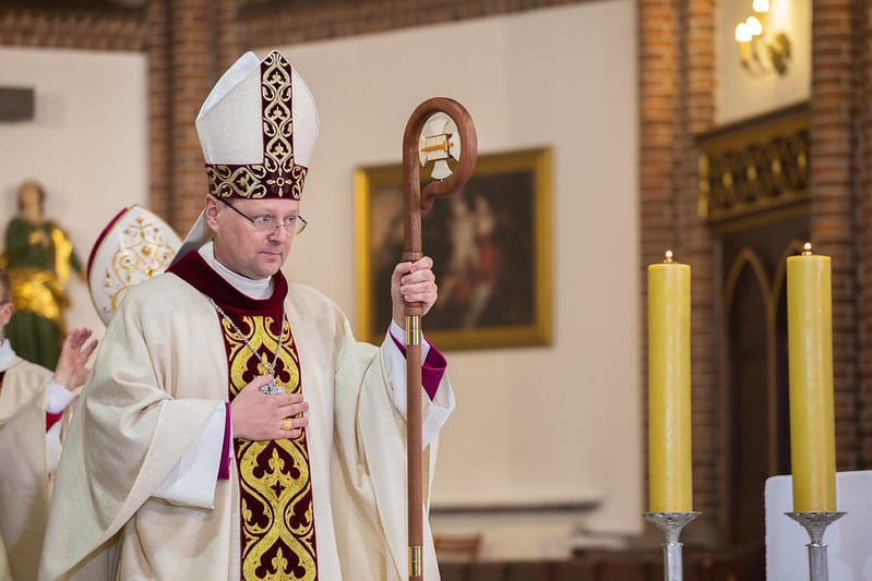 Biskup w mitrze i szatach trzyma pastorał podczas ceremonii religijnej.