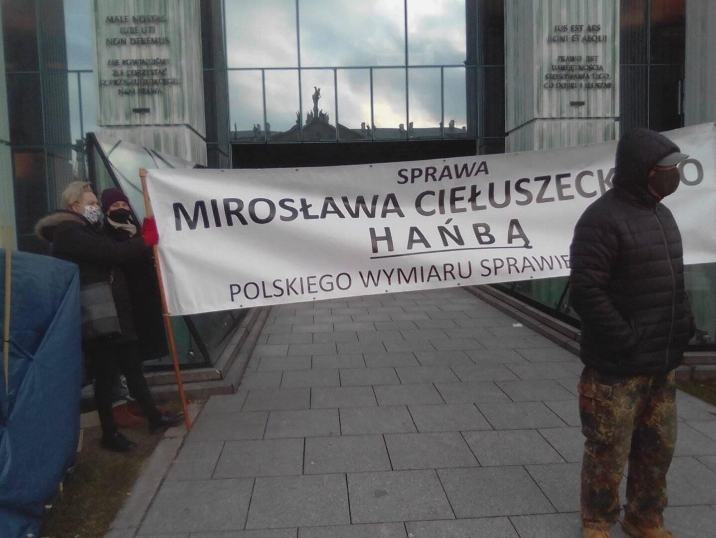 Protestujący trzymają transparent z napisem „Sprawa Mirosława Ciełuszecko – Hańba Polskiego Wymiaru Sprawie”, krytykującym polski system prawny.