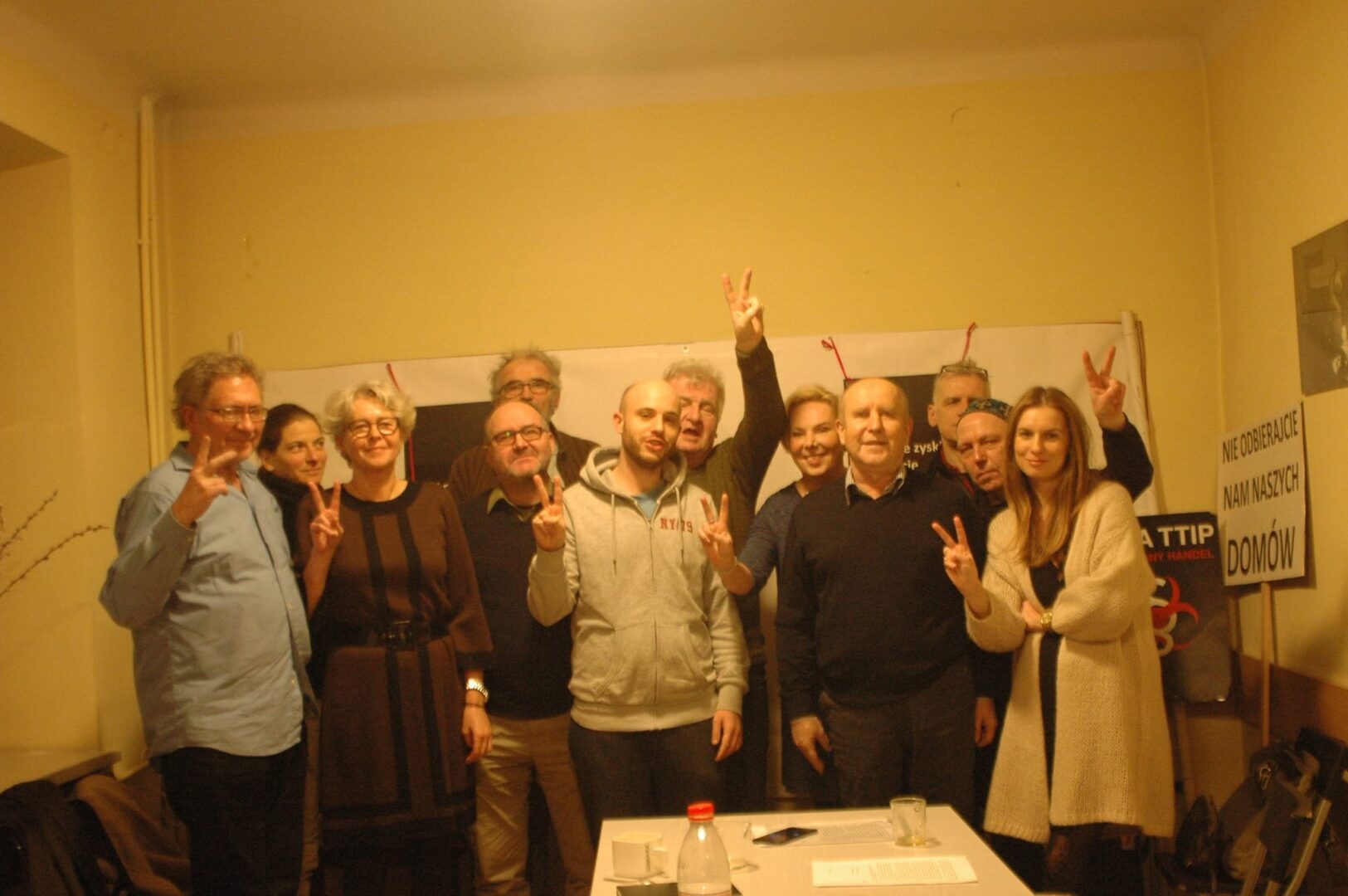 Group of activists protesting housing issues, holding peace signs. "NIE ODBIERAJCIE NAM NASZYCH DOMÓW" sign visible.
