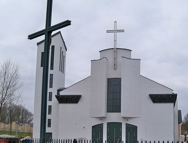 Nowoczesny biały kościół z wysokim krzyżem, prezentujący współczesną architekturę sakralną.