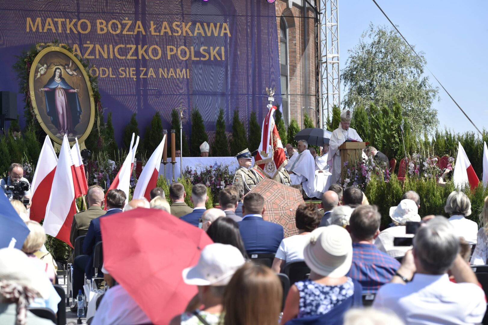 Outdoor religious ceremony with Polish flags and clergy. "Matko Boża Łaskawa Królicznko Polski" banner visible.