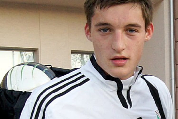 Młody piłkarz w dresie Adidas, patrzący w kamerę.