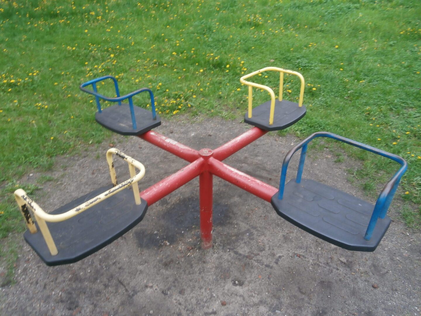 Karuzela na placu zabaw z czterema siedziskami w kolorze niebieskim, żółtym i kremowym.