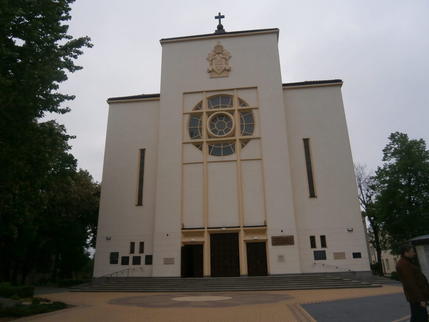 Zewnętrzna część współczesnego kościoła z dużym oknem rozetowym i herbem papieskim. Triduum Paschalne.