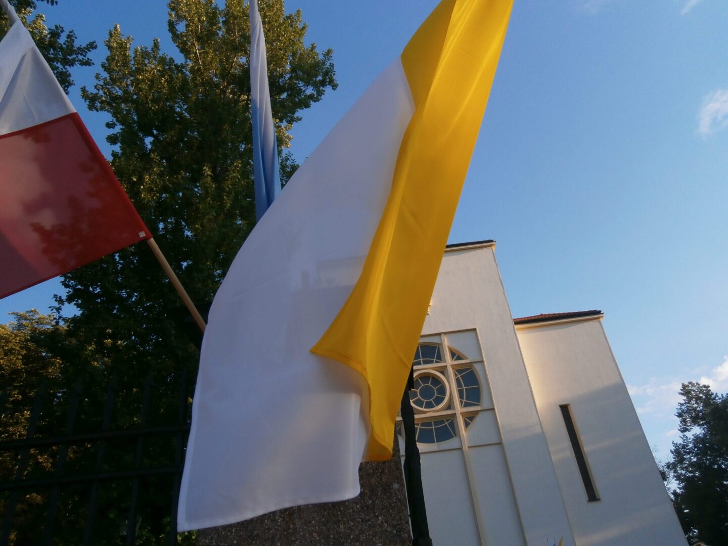 Flagi powiewające w pobliżu białego kościoła z okrągłym oknem.