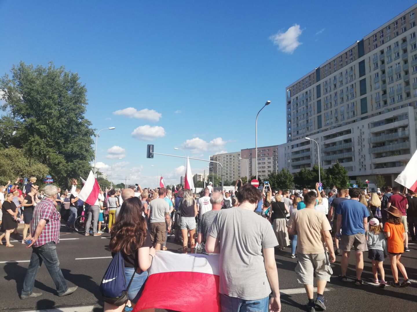 Duży tłum ludzi maszerujących ulicą miasta, trzymających polskie flagi.