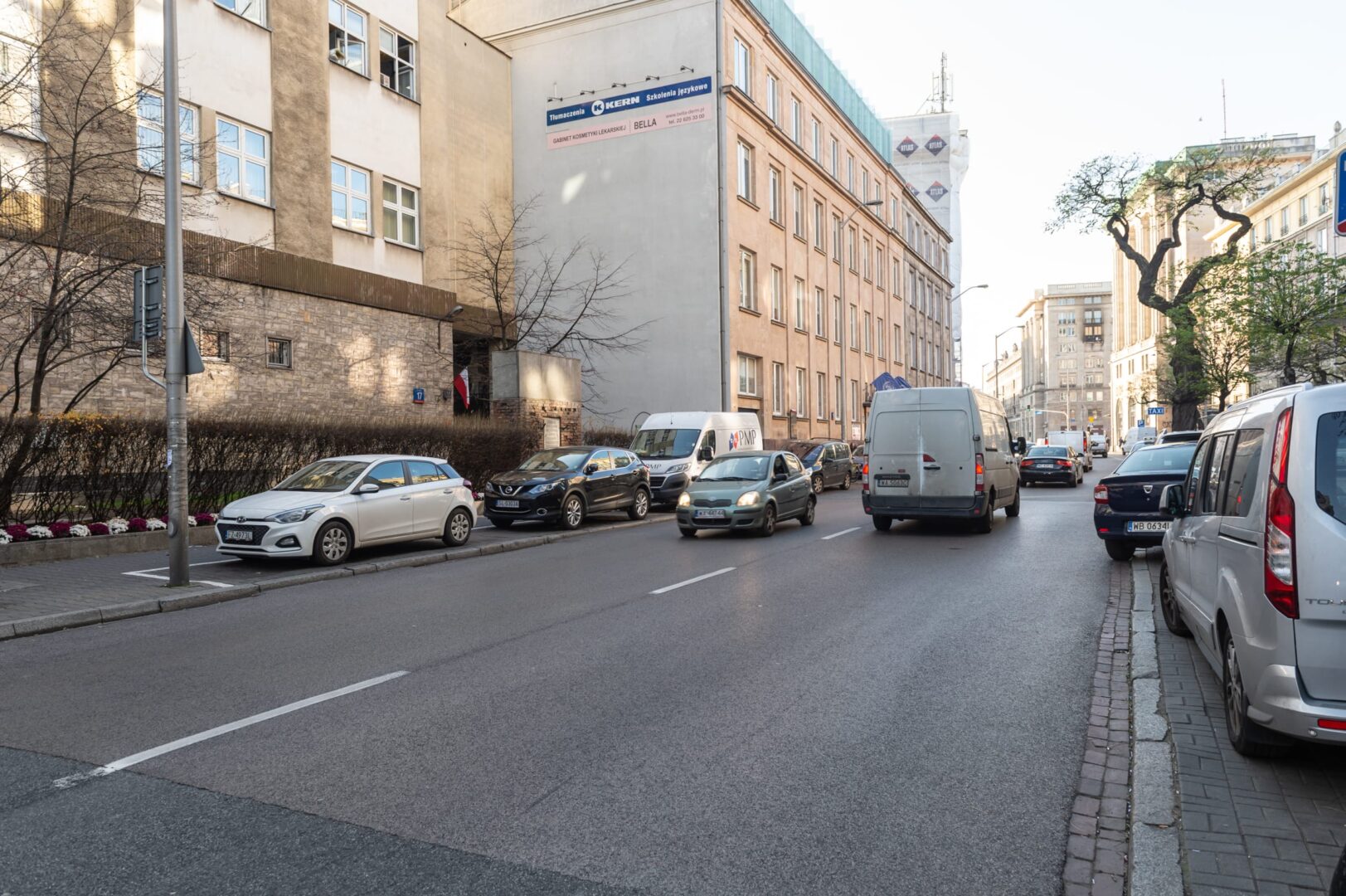 Scena uliczna w Warszawie. Samochody zaparkowane i przejeżdżające obok budynków.