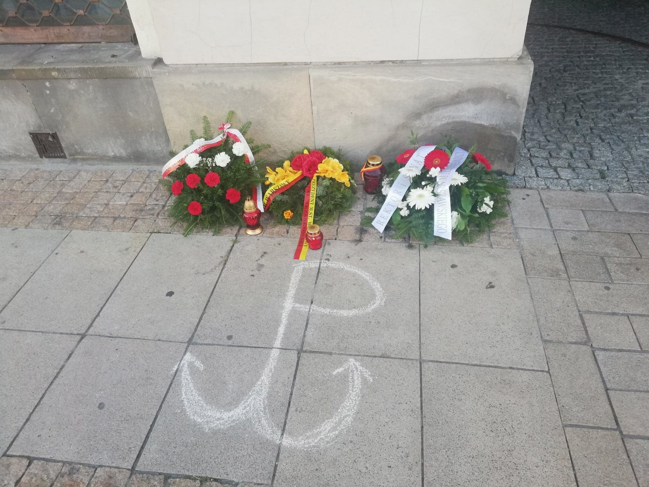 Wieńce pamiątkowe i kotwica narysowana kredą w polskim miejscu pamięci.