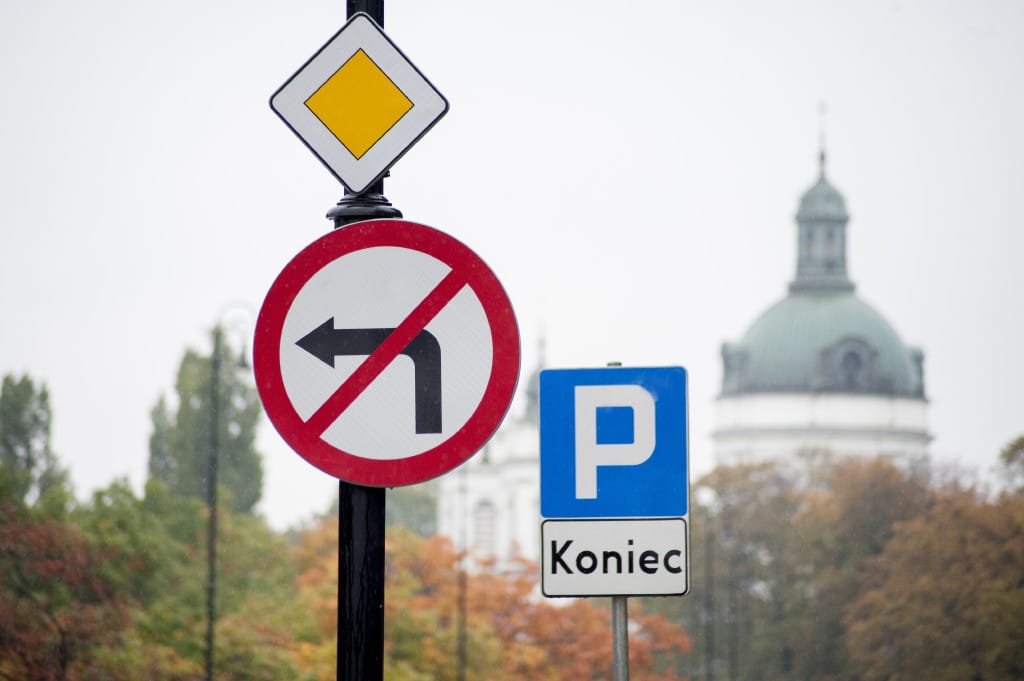 Znaki zakazu skrętu w lewo i końca parkingu na słupie, kościół w tle