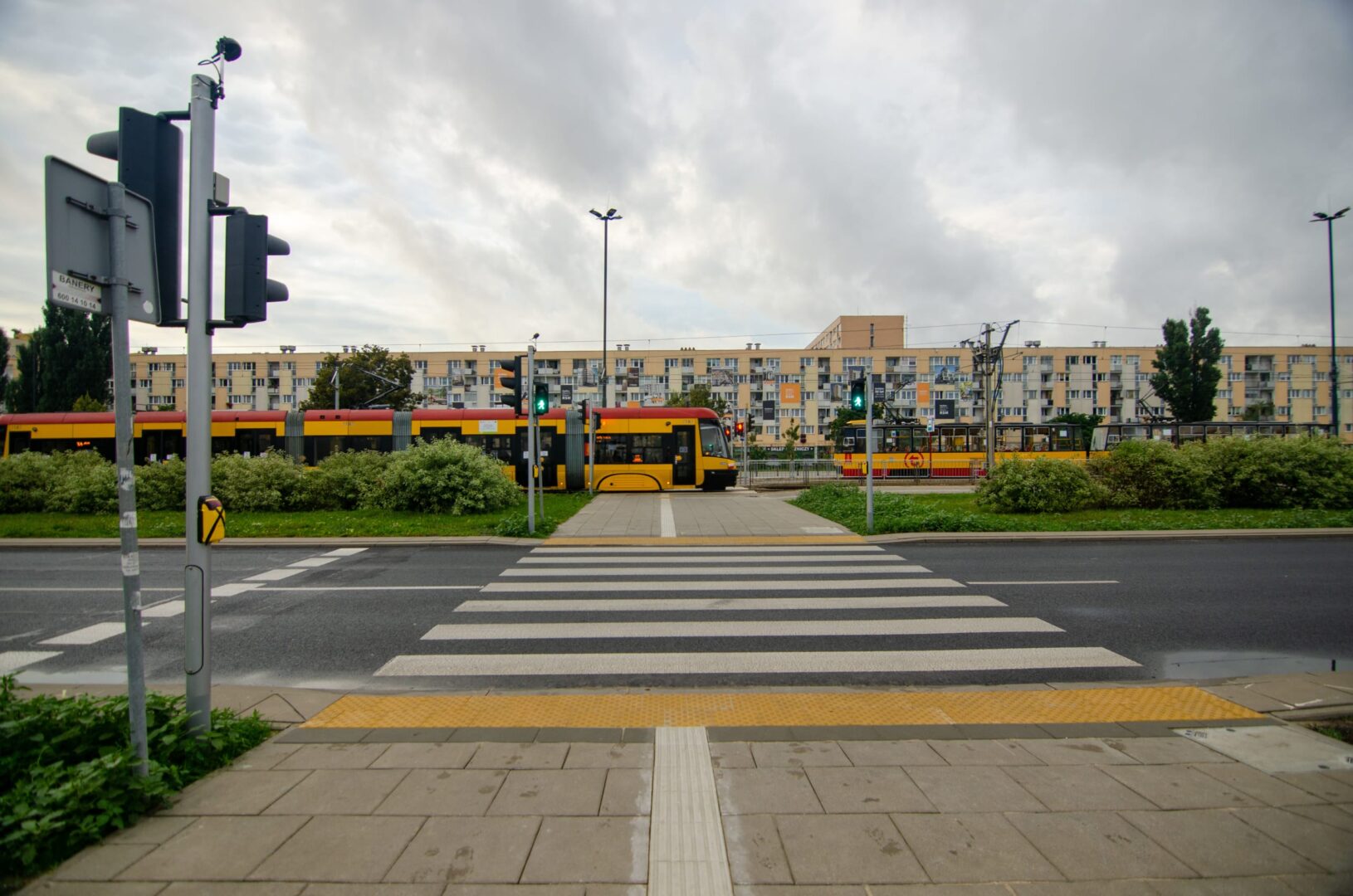 Żółte tramwaje na przejściu dla pieszych przed budynkami mieszkalnymi.