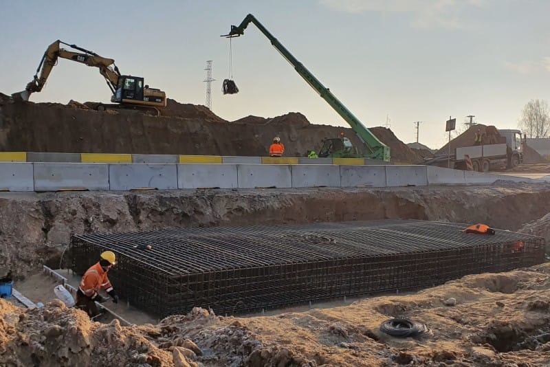 Plac budowy z koparką, dźwigiem i klatką zbrojeniową dla Południowej Obwodnicy Warszawy. Nowy wykonawca w pracy.