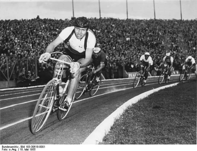 Czarno-białe zdjęcie kolarza prowadzącego grupę podczas wyścigu torowego.