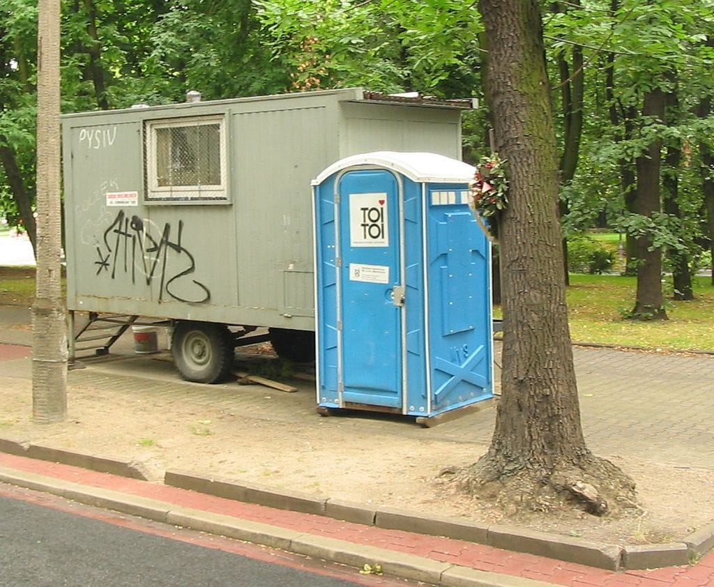 Przenośna toaleta obok przyczepy pokrytej graffiti w parku.