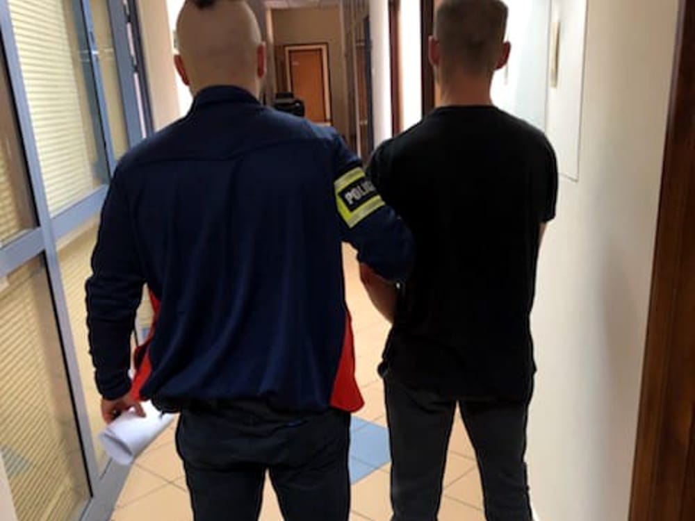 Policjant eskortujący podejrzanego korytarzem.