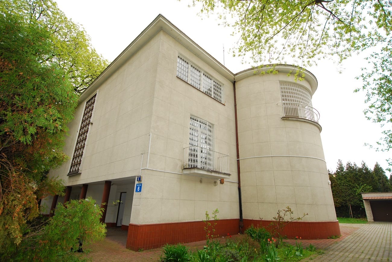 Nowoczesna architektura: Beżowy dom z zakrzywioną fasadą, balkonem i zakratowanymi oknami.