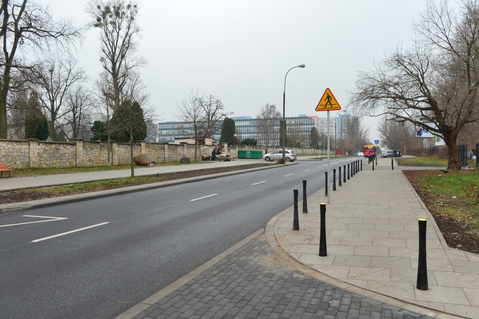 Pusta ulica miasta z chodnikiem dla pieszych, słupkami drogowymi i znakiem przejścia dla pieszych.