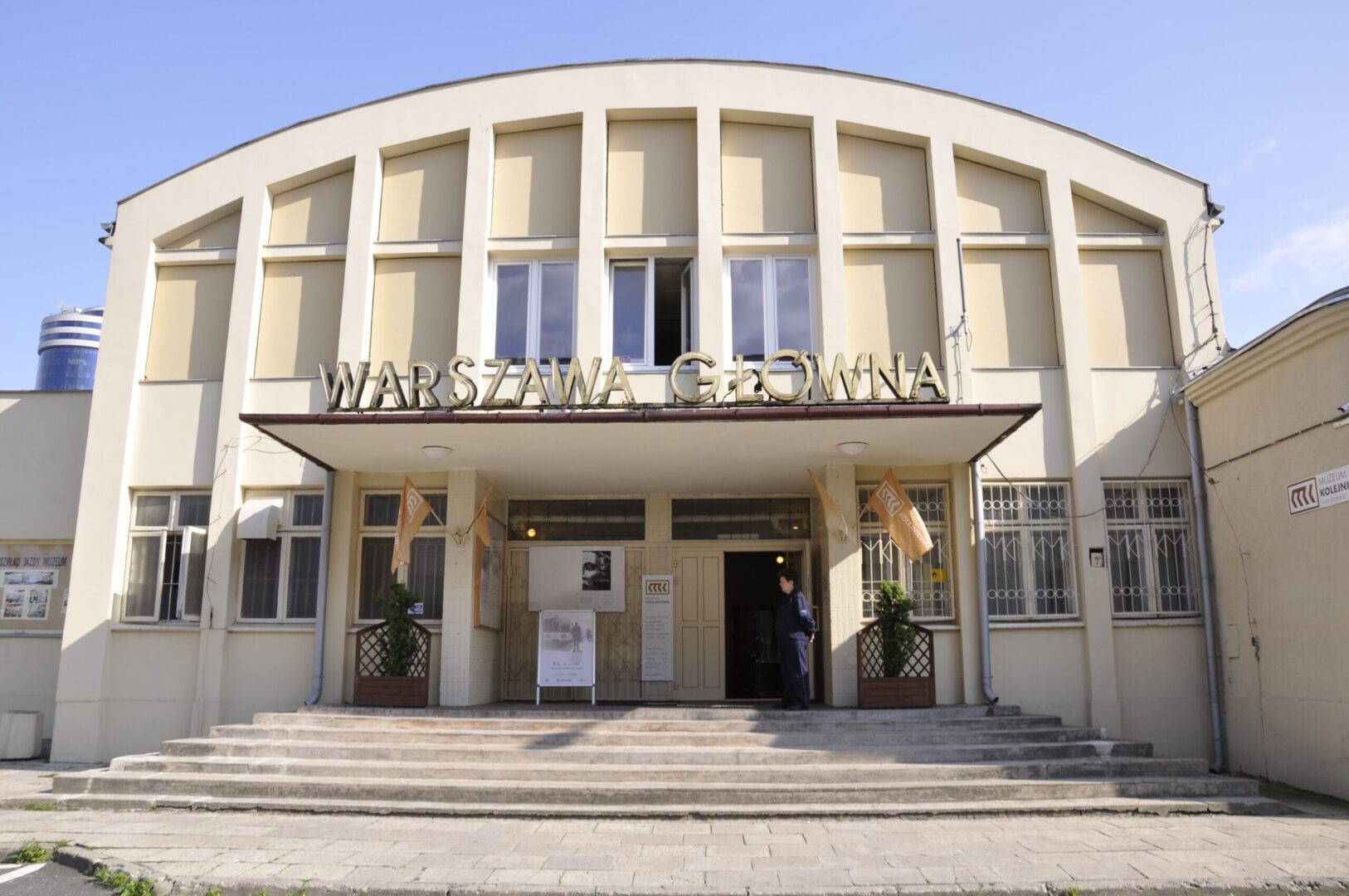 Wejście na dworzec kolejowy Warszawa Główna z łukową fasadą i oznakowaniem.