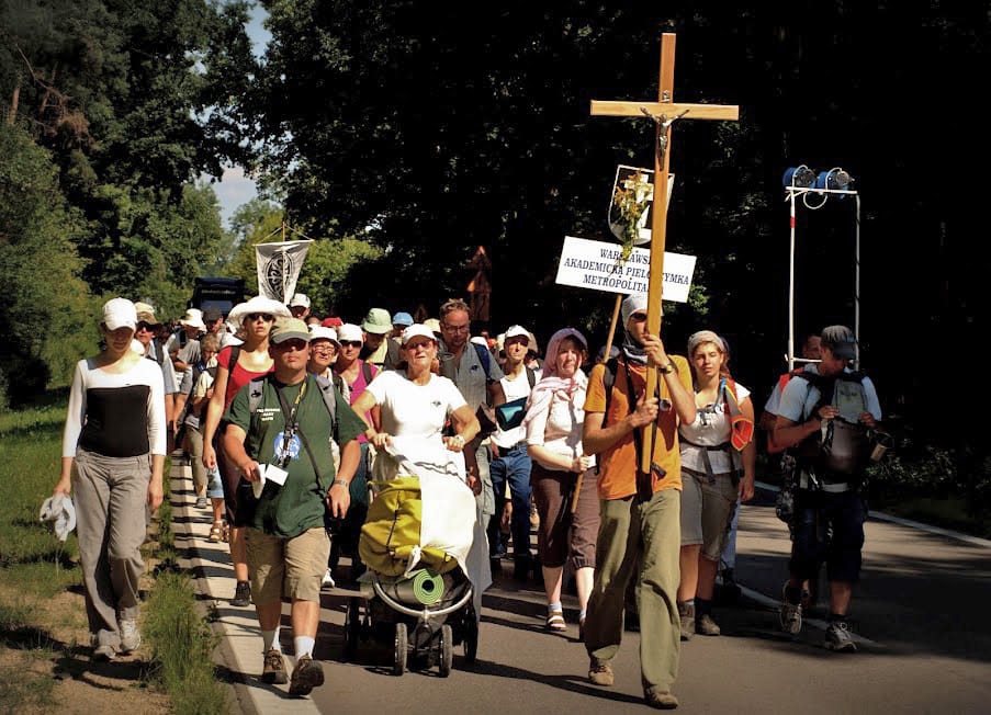 Duża grupa pielgrzymów idących, niosących krzyż i znaki. Procesja religijna.