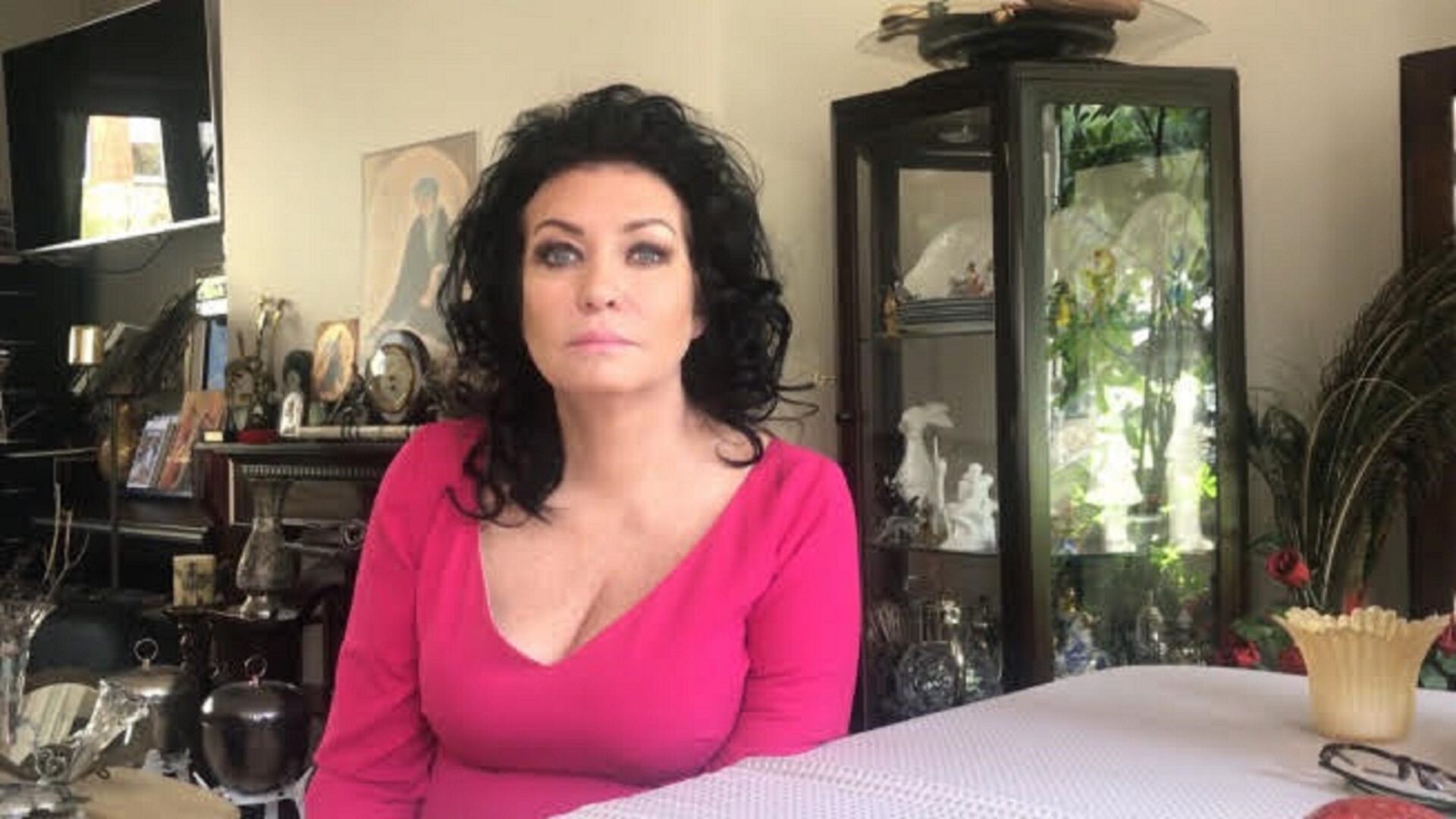 Kobieta w różowym topie siedzi przy stole, otoczonym antycznymi meblami.