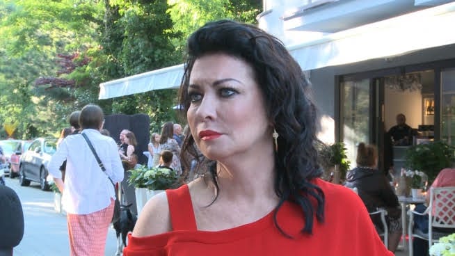 Kobieta w czerwonej sukience uśmiecha się w kawiarni na świeżym powietrzu.