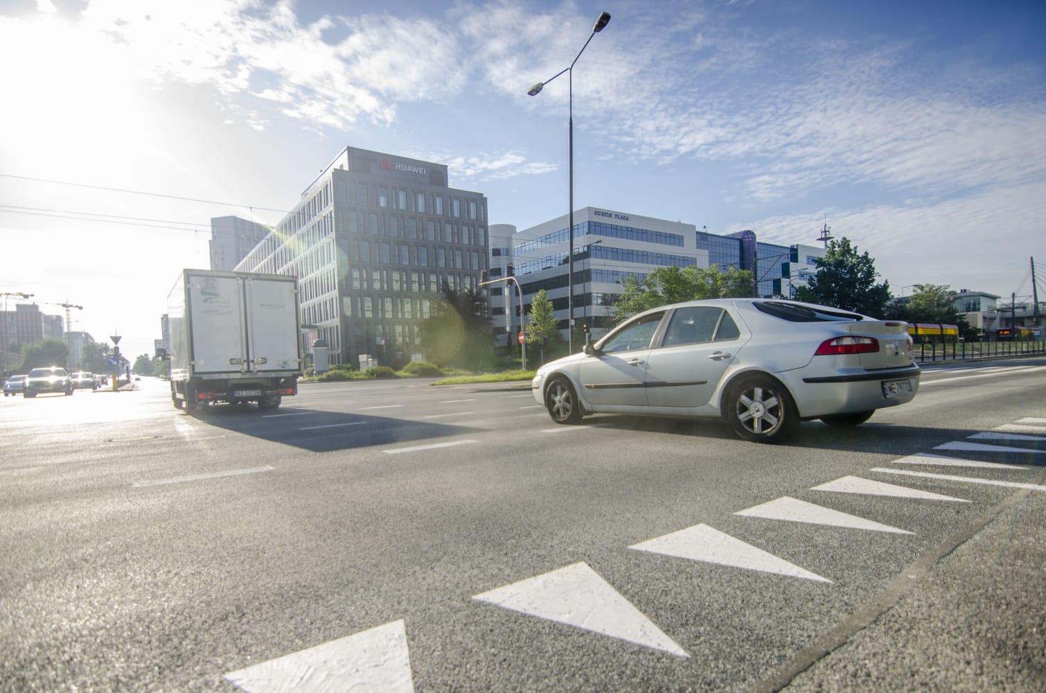 Srebrny samochód przejeżdżający obok nowoczesnych budynków biurowych na miejskiej ulicy.
