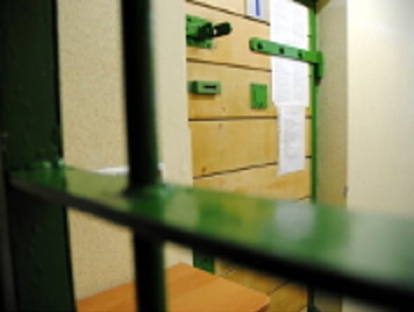 Zielone metalowe kraty i drzwi celi, na których wisiały jakieś dokumenty.