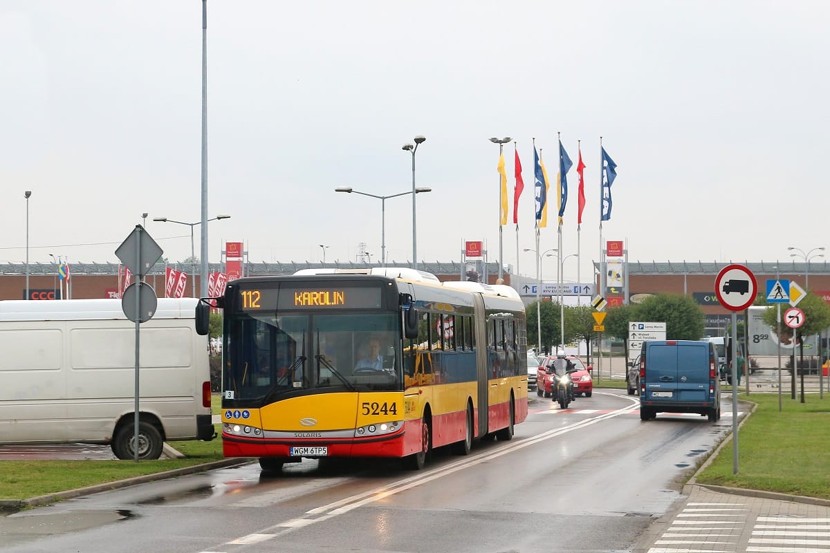 Żółty i niebieski autobus miejski, numer 5244, na linii 112 do Karolin, jadący ulicą miasta.