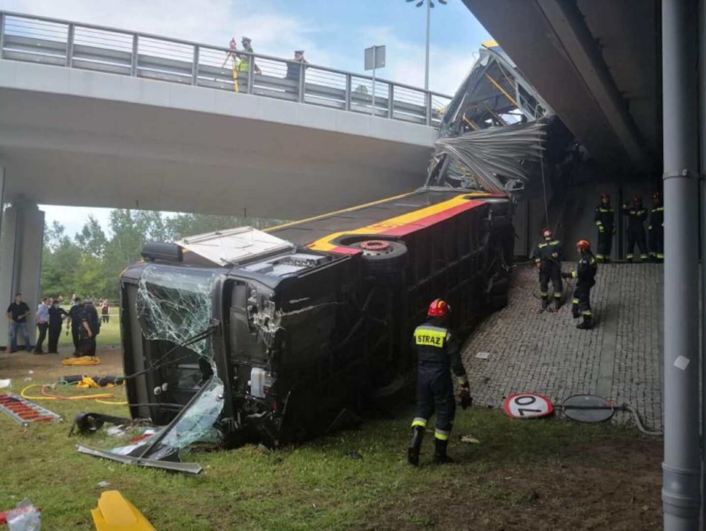 Skutki wypadku autobusowego: przewrócony autobus pod mostem, strażacy na miejscu.