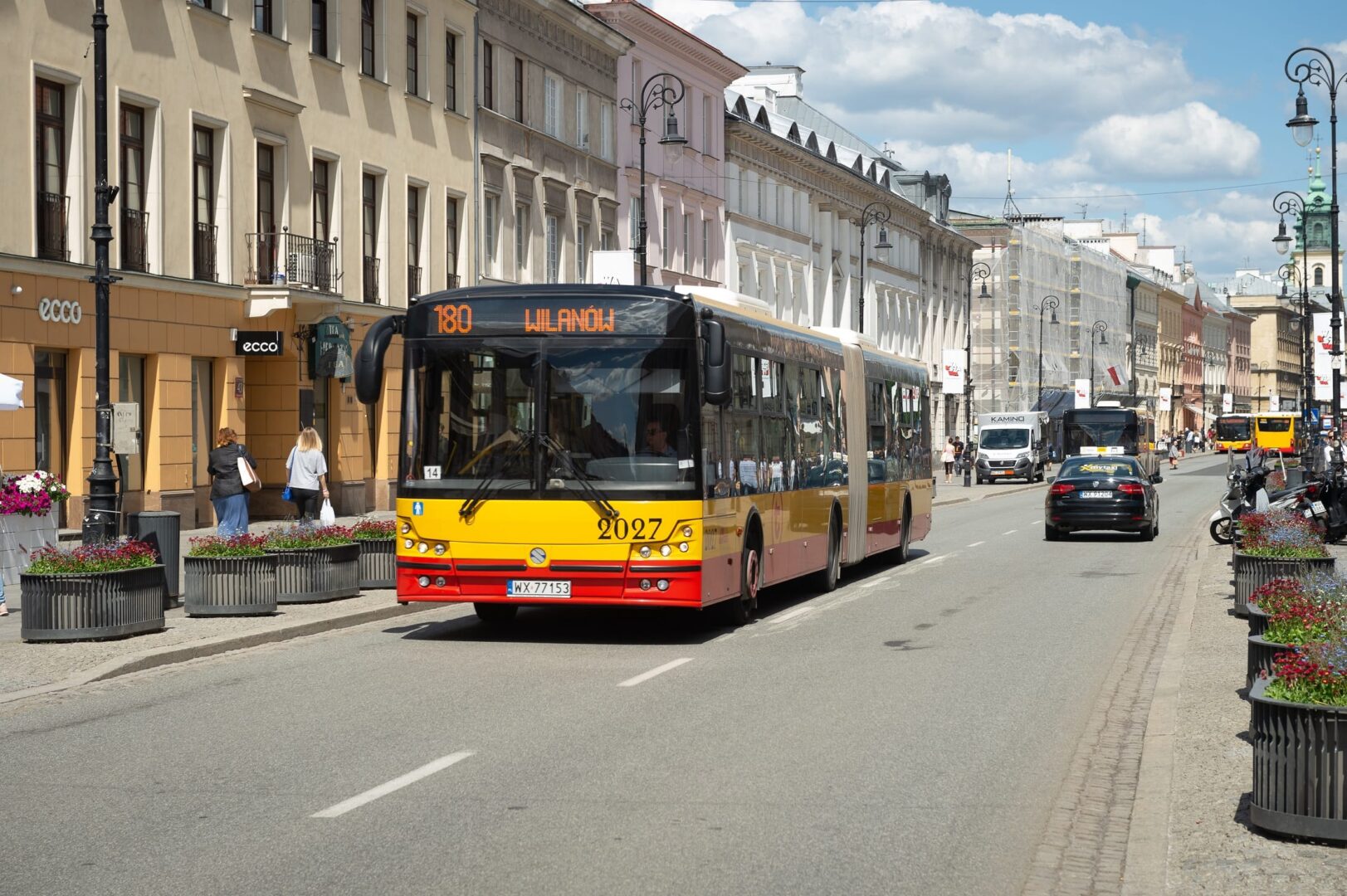 Warszawa, Polska: Żółty i czerwony autobus miejski (linia 180, Wilanów) na nasłonecznionej ulicy.
