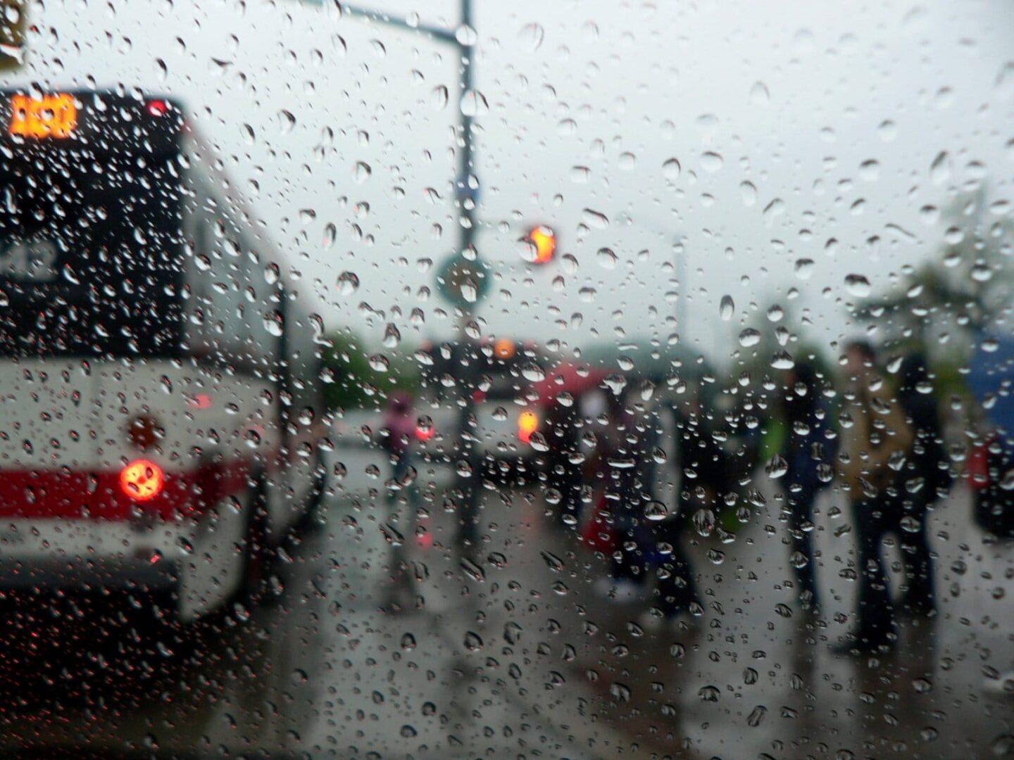 Widok z deszczowej szyby samochodu na autobus i pieszych; niewyraźnie widać.