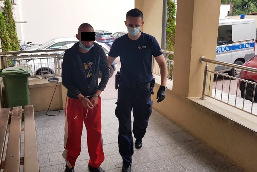 Policjant eskortujący podejrzanego w kajdankach. POLICJA.