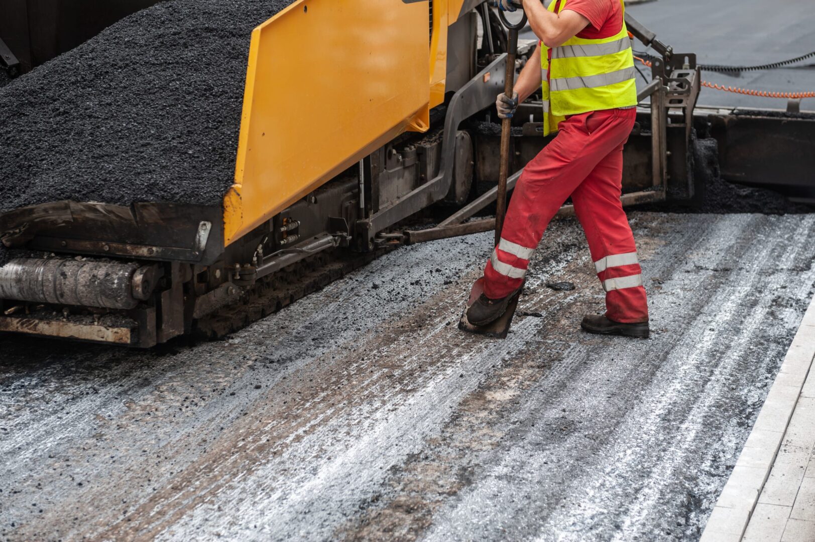 Robotnik drogowy używa łopaty do wyrównywania asfaltu podczas układania nawierzchni drogi